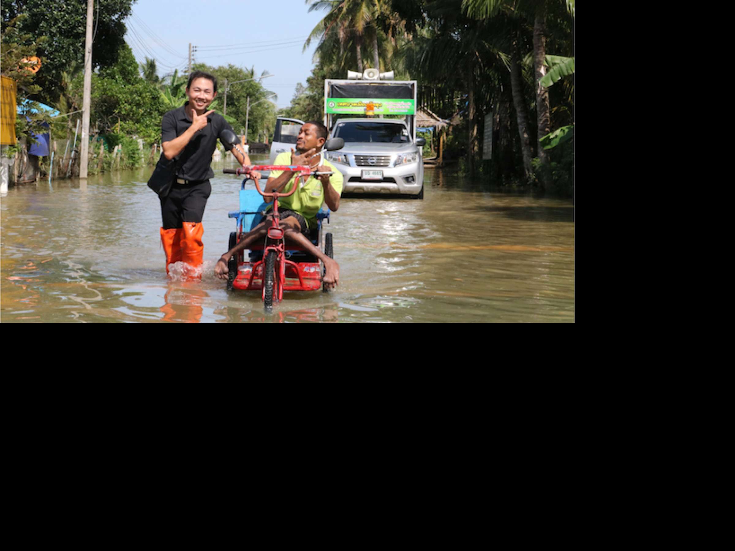 a volunteer  help disable man with his wheel chair walk through flood and he still smile.