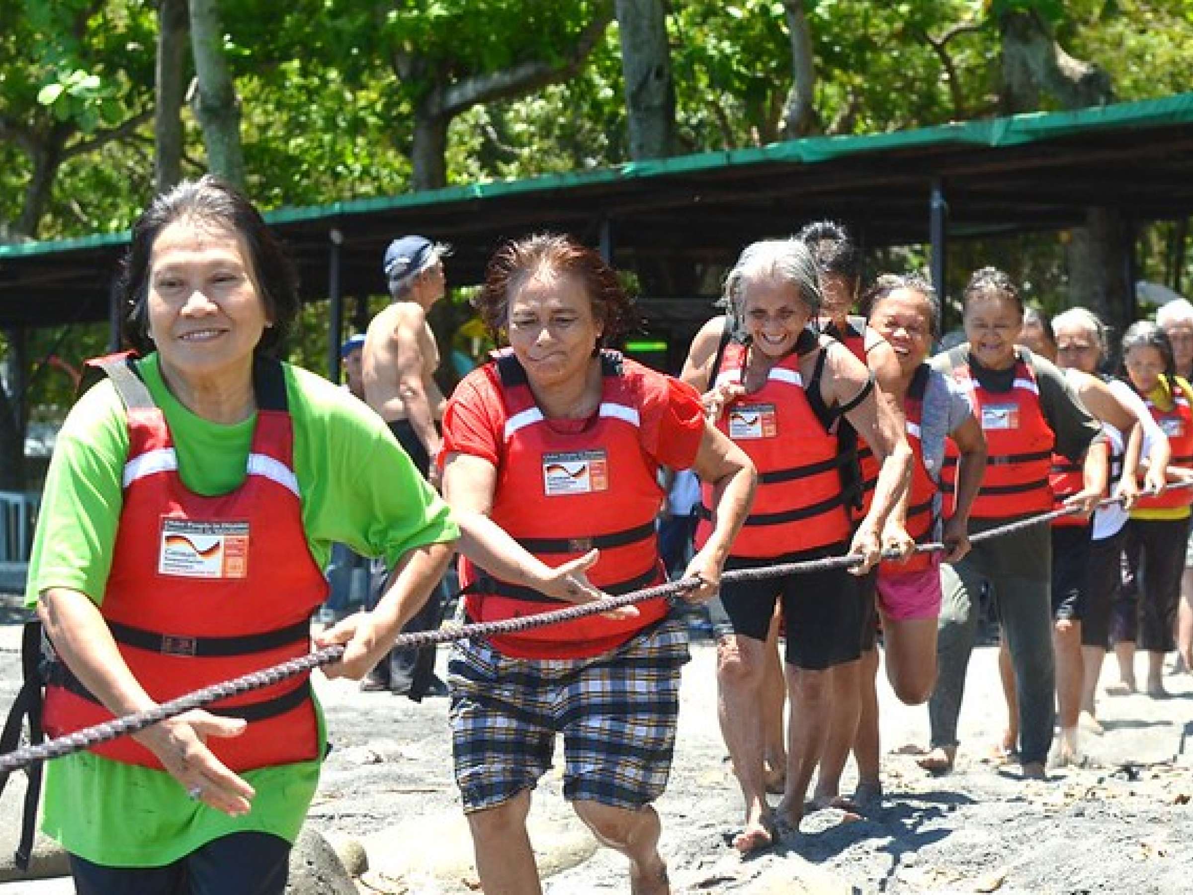 group of people wearing life vests run holding a rope and smiling