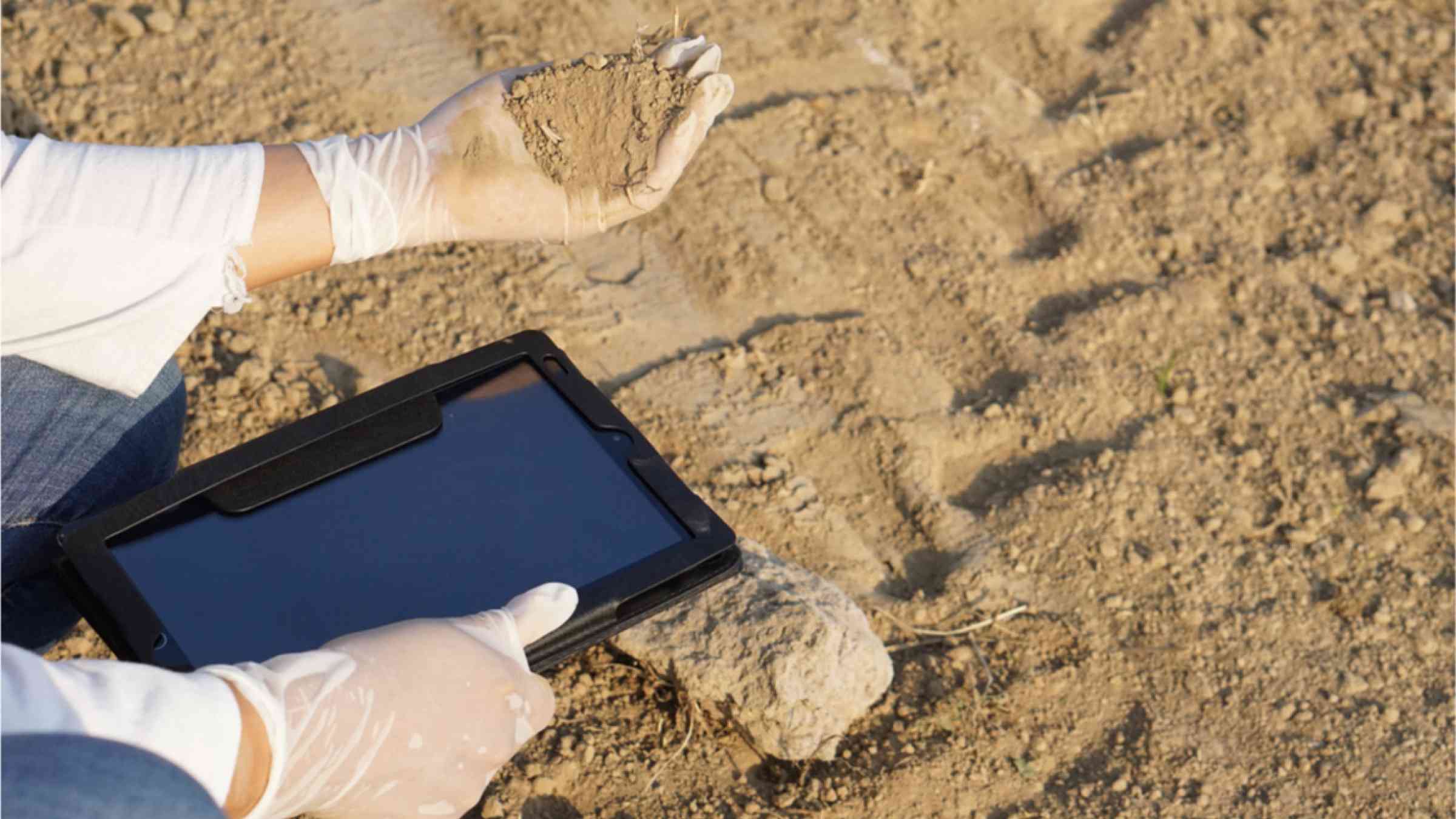 Hands holding smart tablet and soil. Concept about using digital wireless technology to research and collect data about agriculture problem. Checking soil quality before growing plants.