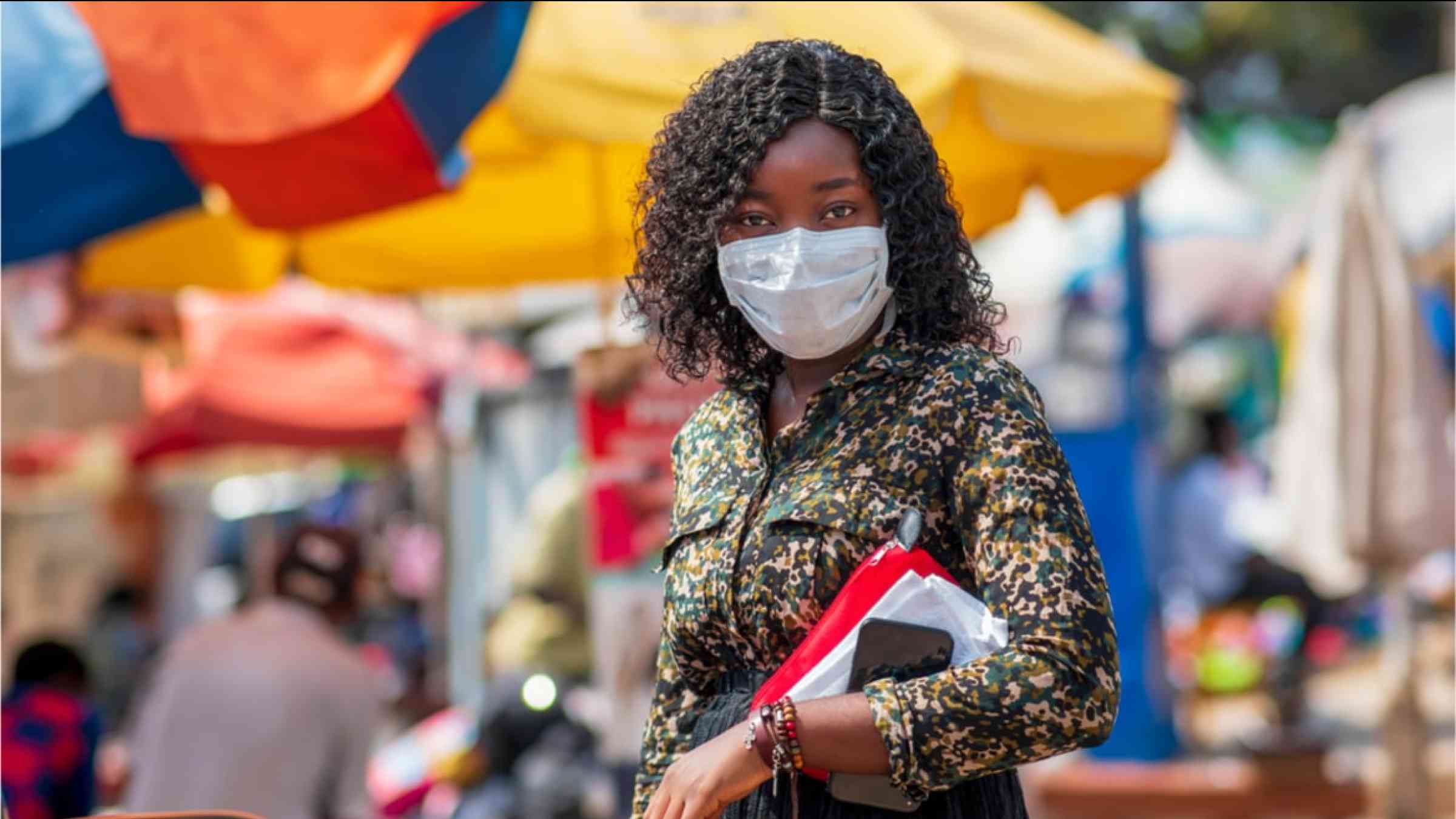 AN African woman wearing a face mask to protect her from COVID-19. She is walking across a market.