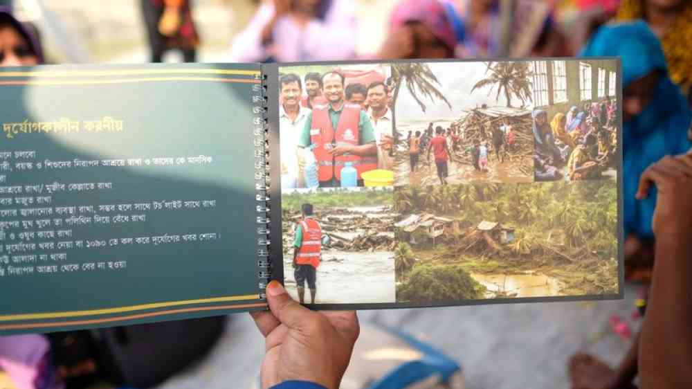 Person showing book about disaster preparedness and response measures and pictures taking place in Bangladesh.