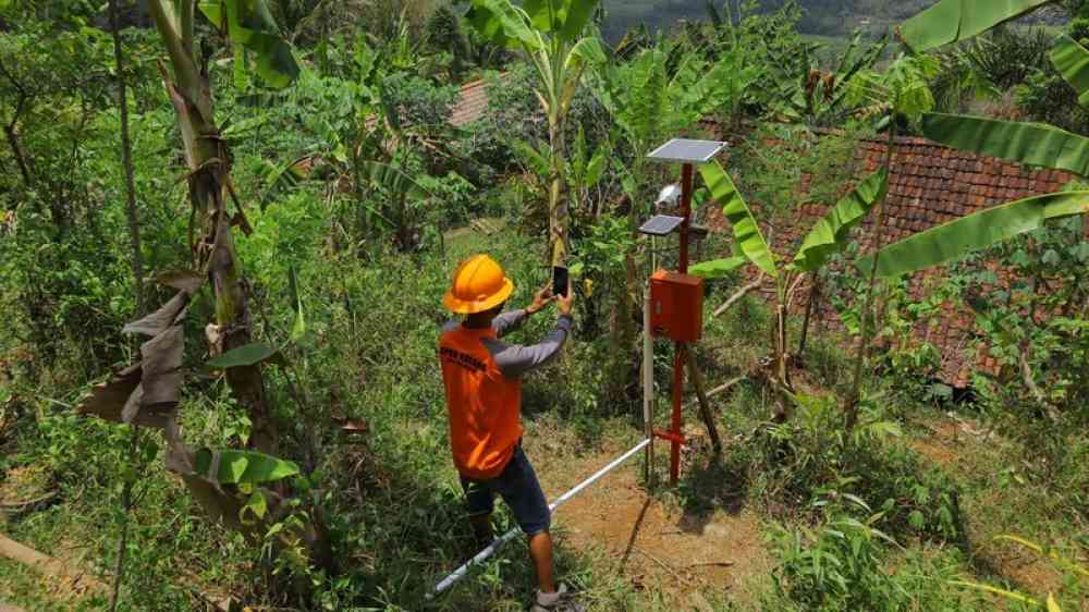 Worker uses a smartphone to document the condition of the solar panel for a landslide early warning system on a rural hill slope near Magelang, Indonesia.