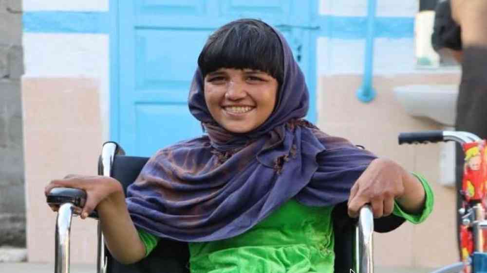 A young girl in a green dress smiles while sitting in her new wheelchair at an assistive devices distribution event