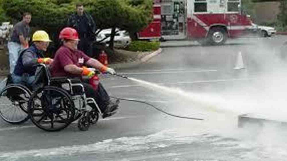 Person in wheelchair using a fire extinguisher in a training exercise