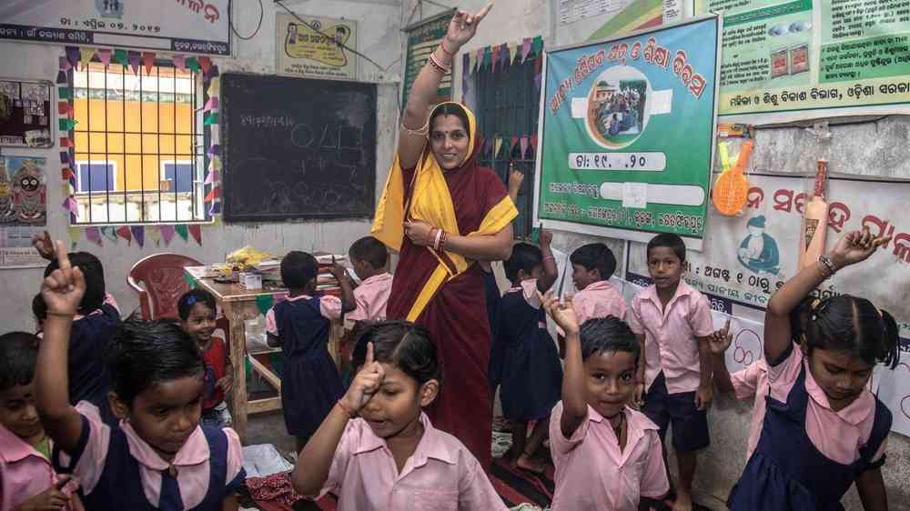 A class of schoolchildren and their teacher in India raising their fingers in the air during a disaster preparedness lesson.