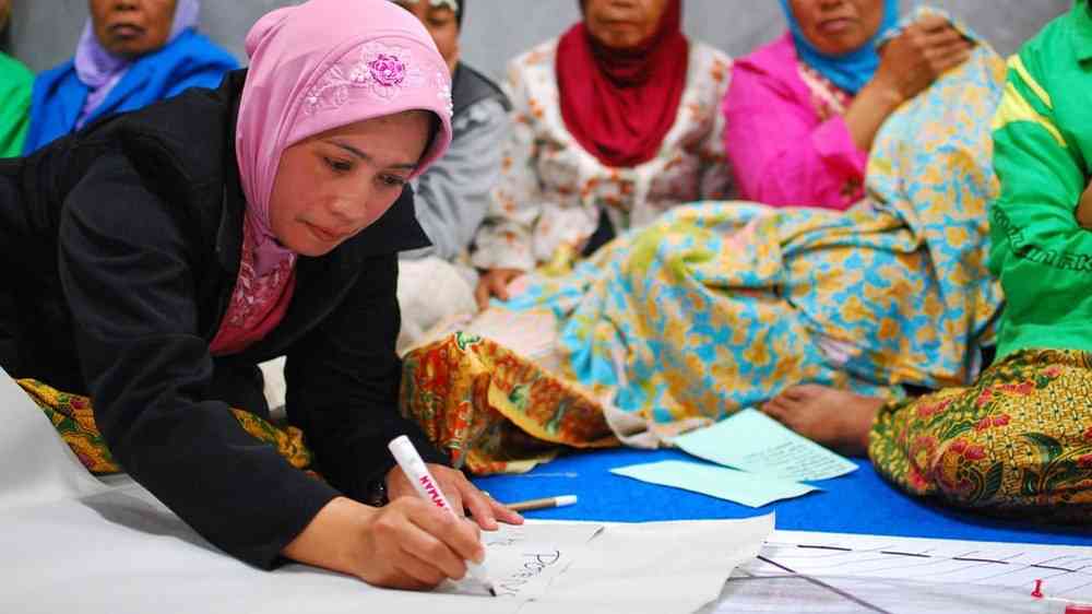 Indonesian woman writing in board paper at community meeting
