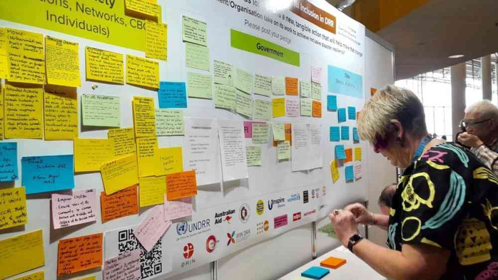 wall covered in post-it notes with pledges and people writing new ones